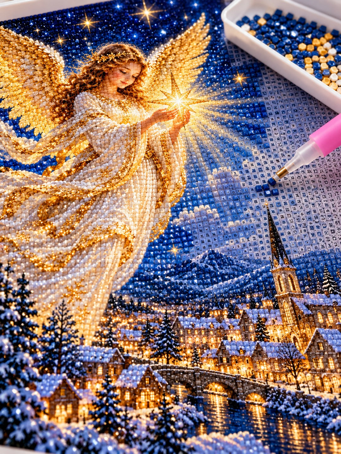 Close-up of the Christmas angel holding a radiant star above a snowy town diamond painting in progress, square resin drills, wax pen and drill tray