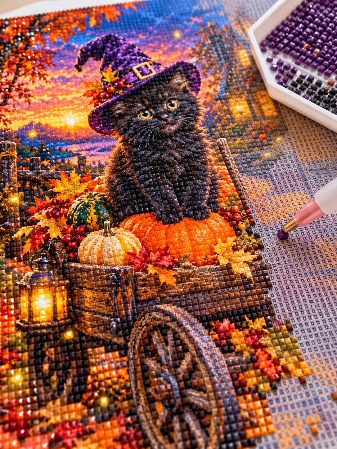 Close-up of the black kitten in a witch hat on a pumpkin cart diamond painting in progress, square resin drills, wax pen and drill tray