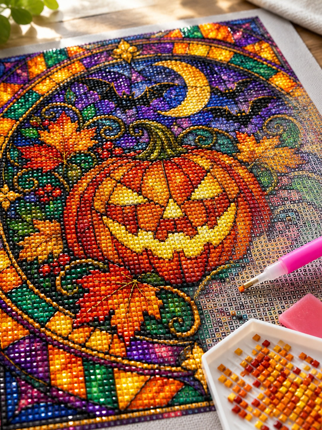 Close-up of the stained glass jack-o'-lantern window with bats and moon diamond painting in progress, square resin drills, wax pen and drill tray